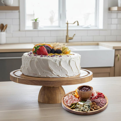 Wooden cake stand with glass cover displaying a cake, next to a charcuterie board.